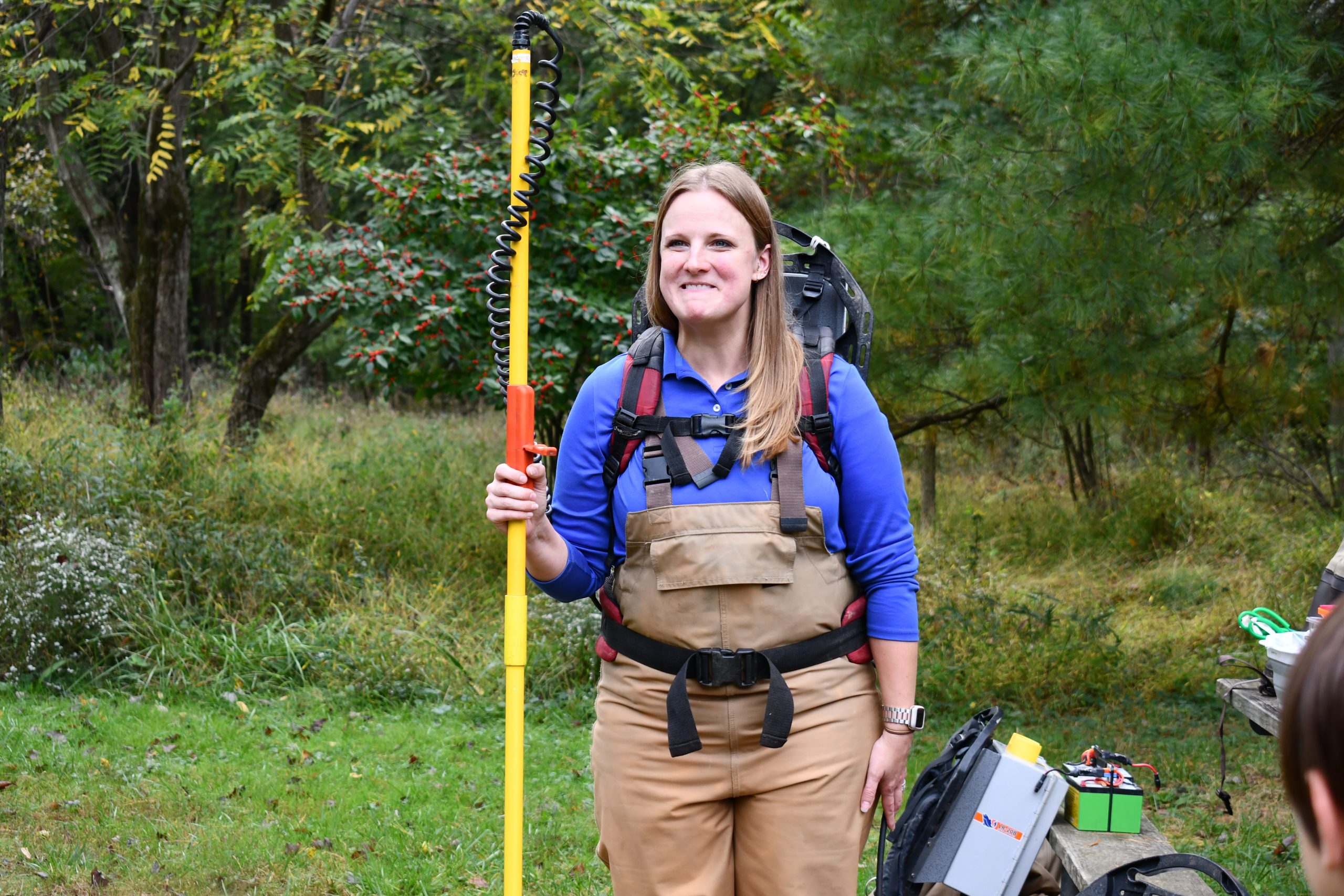 Rachel Gauza Gonert stands in Maydale Nature Center in waders and hold water surveying equipment.