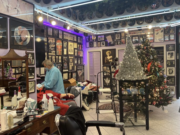 Salon owner washes client's hair in front of photo-covered walls and a Christmas tree.